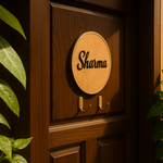 Wooden door with a circular MDF plaque displaying 'Sharma' and two hooks, surrounded by green leaves.