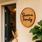 MDF  round board  with 'Sharma Family' text on a wall with plants and a door in the background