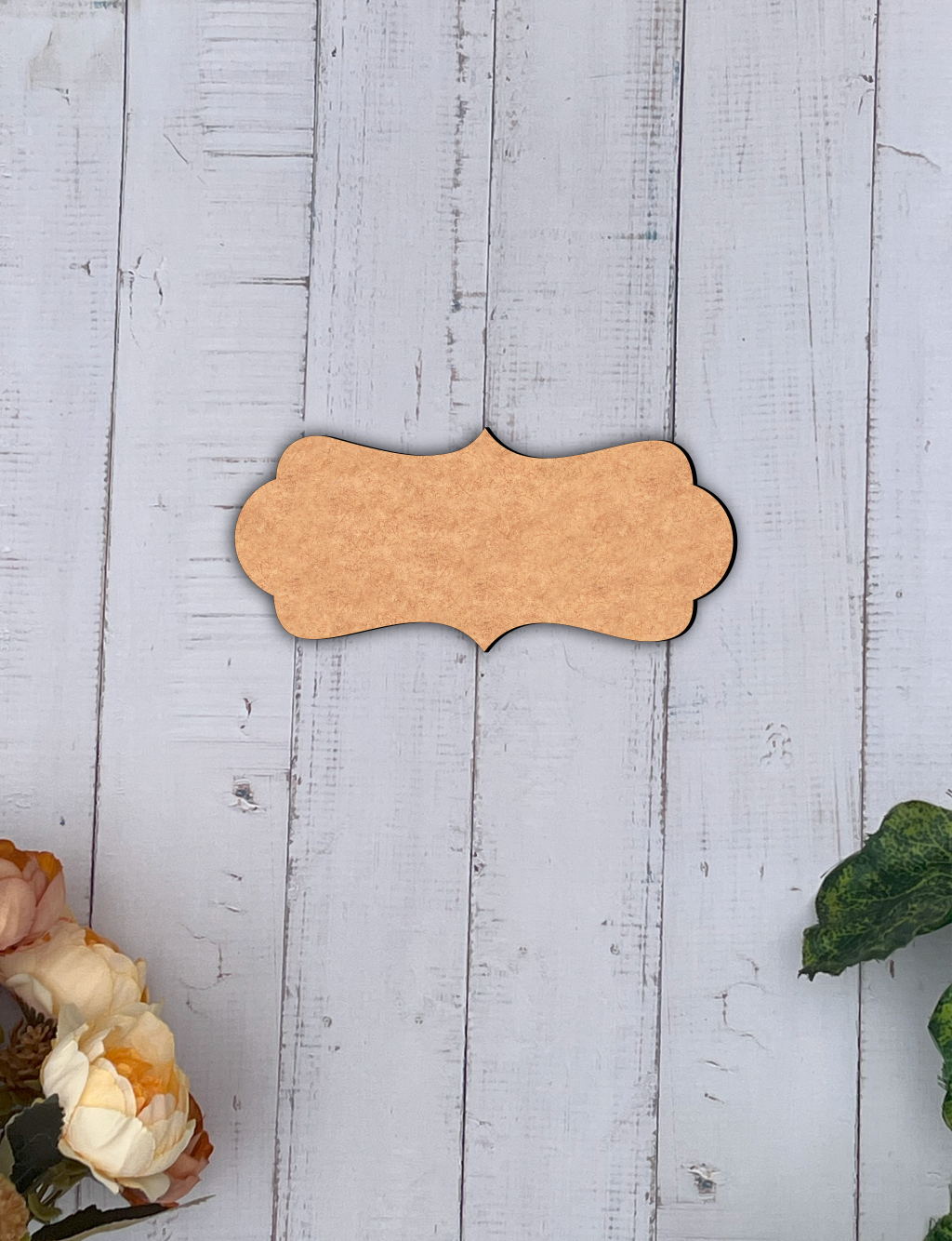 MDF board nameplate on a light wooden surface with floral and green leaf decorations.