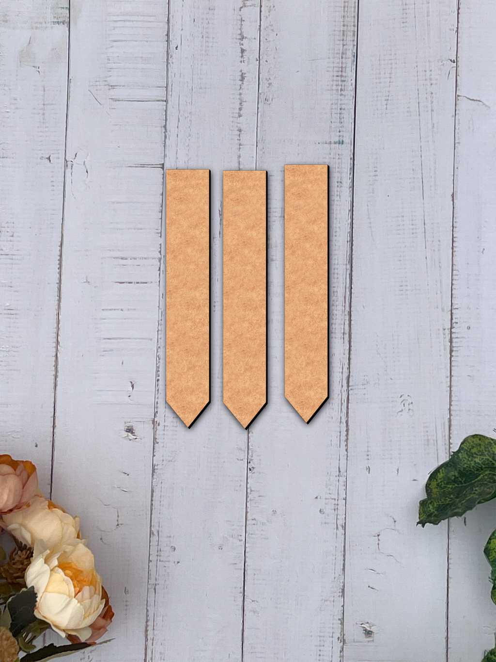 Three MDF board rectangular objects on a light wooden surface with floral and leaf decorations.