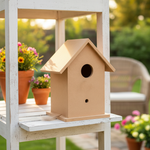 Unpainted MDF birdhouse with slanted roof on white wooden shelf, garden view