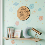 Round wooden cutout with space-themed design and 'Kian' engraved, on a light wooden background.
