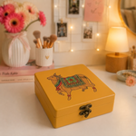 Yellow DIY MDF Lock box with a pichwai cow illustration on a desk with flowers and books in the background