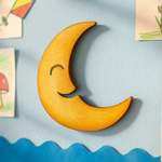 Painted yellow MDF crescent moon wall hanging displayed on blue wall with kids drawings