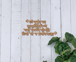 MDF Shloka wall art featuring the Gayatri Mantra in a laser-cut style, mounted on a white painted wooden plank wall with green plant leaves in the lower right corner.