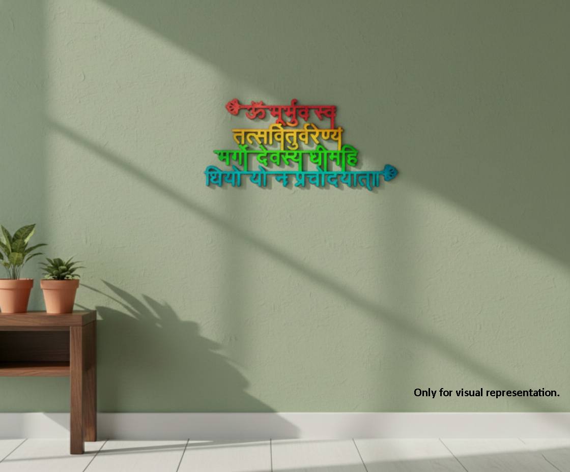 A shloka wall sign with Devanagari script in red, orange, green, and blue, mounted on a sage green wall. The scene includes a wooden side table with two potted plants on the left and soft window shadows cast across the wall and floor.