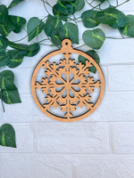Round DIY MDF floral snowflake ornament cutout with hanging loop, paintable Christmas craft mounted on white bricks wall