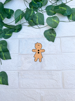 DIY MDF gingerbread girl cutout with bow, smiling face and button details, blank craft shape on white brick wall background.