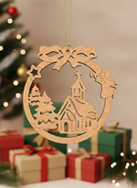 DIY MDF Christmas round ornament cutout with church, trees and angel design, hanging with golden string in front of a decorated Christmas tree and gift boxes.