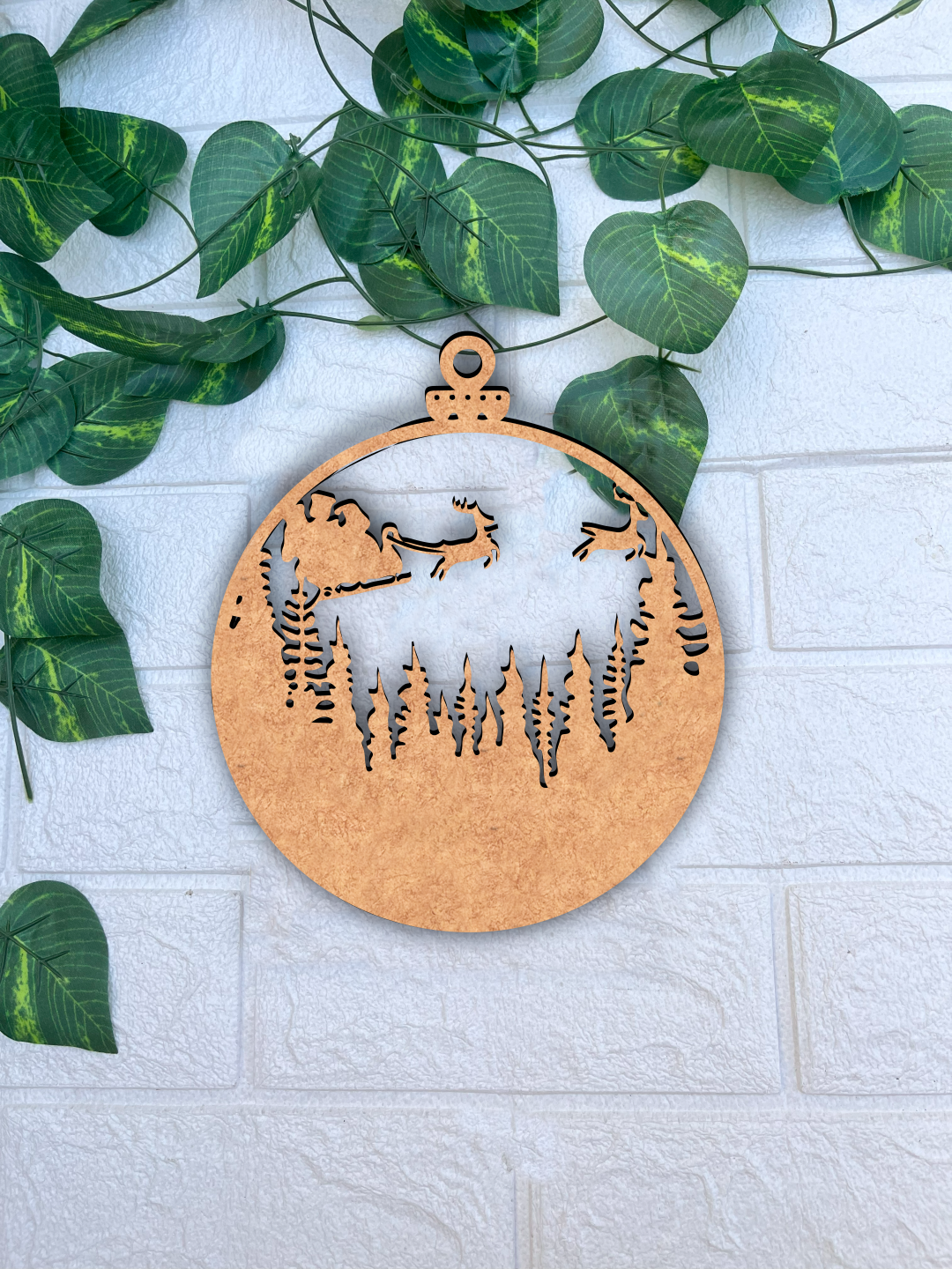 DIY MDF Christmas ornament cutout with Santa sleigh and reindeer for painting and craft placed on a white textured brick wall background with green vine leaves.