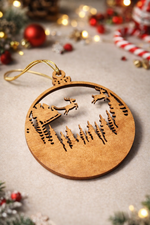 Laser-cut MDF Christmas bauble ornament featuring Santa’s sleigh and reindeer over a pine forest scene, with hanging cord and festive holiday decor background.
