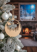 Laser-cut MDF Christmas bauble ornament with Santa sleigh and reindeer design hanging on a snowy Christmas tree, with cozy fireplace and winter window background.