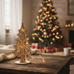 DIY MDF Christmas tree tabletop decor with cutout design and warm fairy lights, placed on a wooden table with a blurred Christmas tree in the background