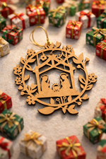 MDF nativity Christmas ornament with Mary, Joseph, and baby Jesus inside a wreath frame, placed on a festive holiday background with decorations and lights.
