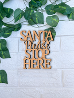 DIY MDF “Santa Please Stop Here” text cutout for Christmas craft mounted on white brick wall
