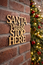 DIY MDF “Santa Please Stop Here” text cutout for Christmas craft mounted on brick wall