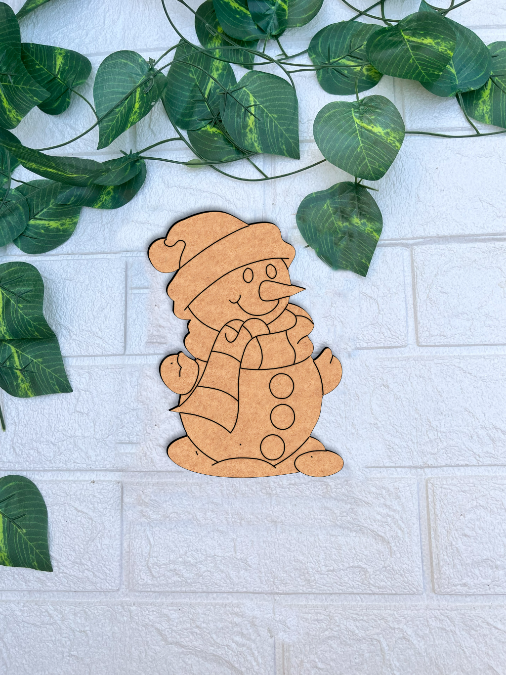 DIY MDF snowman cutout for Christmas craft mounted on white brick wall with green vine leaves 