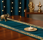 Decorative teal table runner with gold patterns on a wooden table, featuring a lit candle and small statue with mdf tea light candle holder.