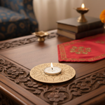 Decorative candle holder with a lit candle on a wooden table with books and a red cloth in the background.