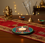 Decorative candle on a colorful plate with incense sticks and a statue of Ganesha on a red cloth and handpainted mdf tea light candle holder.