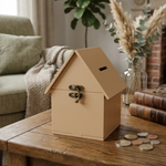 MDF Hut shaped Piggy Bank on a wooden table with coins around, in a cozy living room setting.
