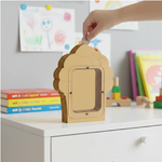 DIY MDF cupcake shaped Money bank  with a hand placing a coin into it, set against a background of books and toys.