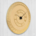 Decorative gold wall clock with Roman numeral design on a light wooden background