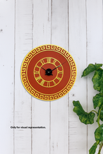 Decorative wall clock with red face and gold border on a white wooden background with green leaves.