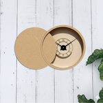 Round Shadow wall clock on a white wooden surface with green leaves.