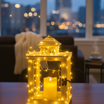 Decorative gold lantern with a lit candle and string lights on a table, blurred cityscape in the background.