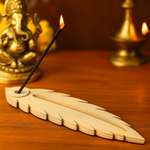 MDF feather incense holder with lit incense stick and marigold petals.