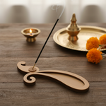 MDF paisley-shaped incense holder on wooden table with lit diyas and marigolds.