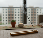 incense holder with burning stick, smoke rising, background showing modern apartment view.