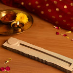 MDF incense holder with wave-edge design on wooden table with diya and flower petals.