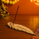 MDF feather-shaped incense holder on wooden surface with diya and rudraksha mala