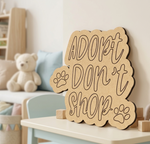 MDF DIY  sign with 'Adopt Don't Shop' text on a table in a room with a teddy bear and cushions.