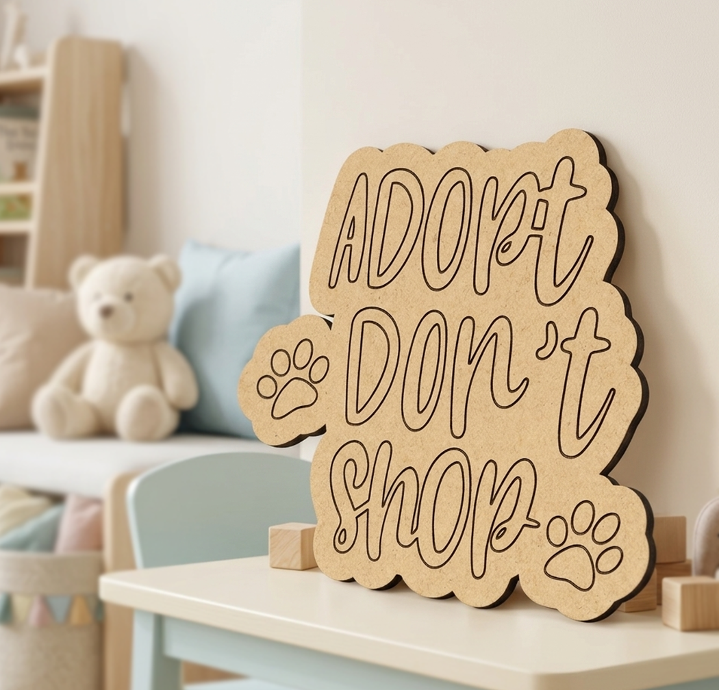 MDF DIY  sign with 'Adopt Don't Shop' text on a table in a room with a teddy bear and cushions.