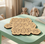 MDF DIY sign with 'Adopt Don't Shop' on a green table with stuffed animals in the background.