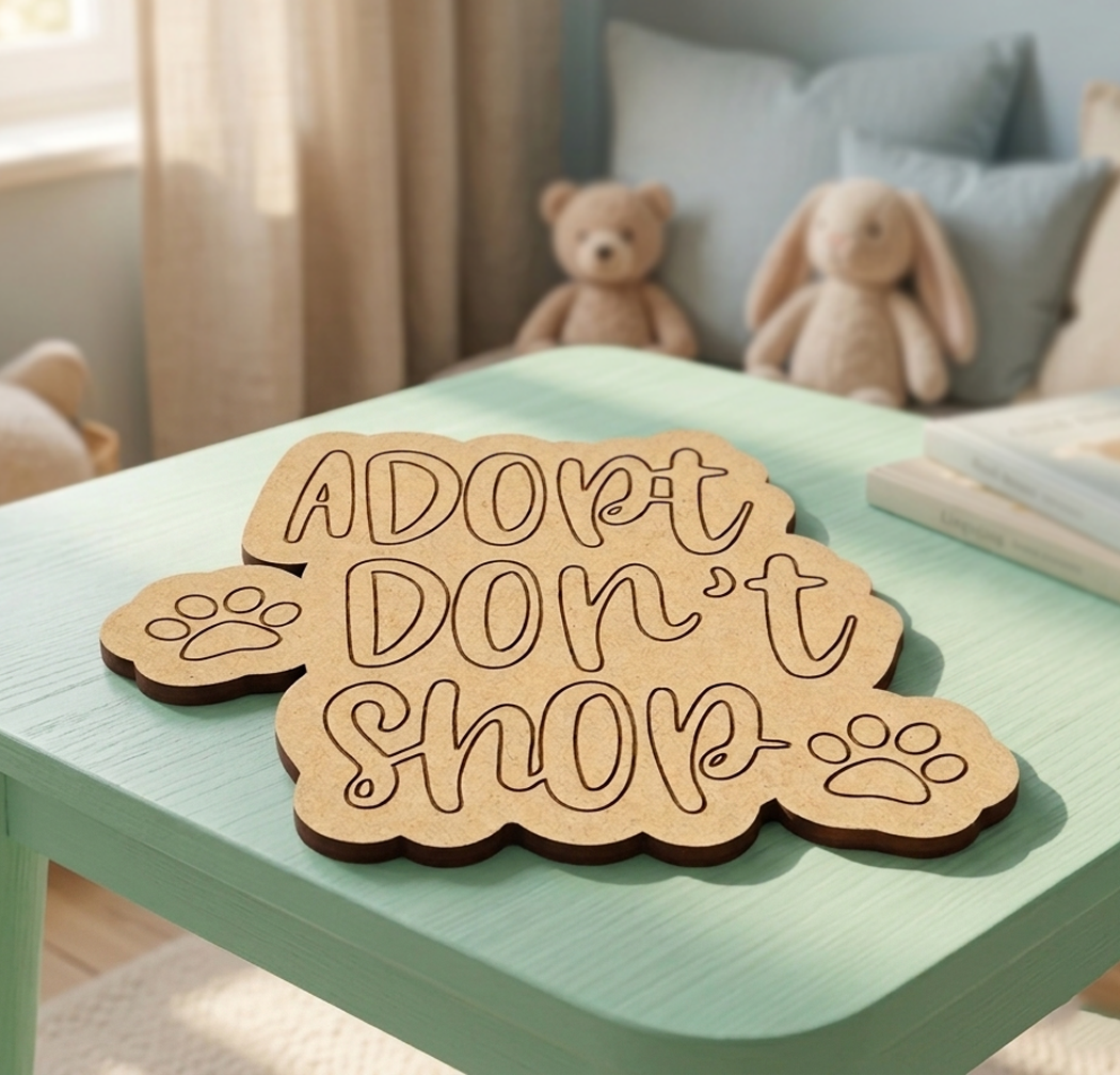 MDF DIY sign with 'Adopt Don't Shop' on a green table with stuffed animals in the background.