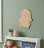 DIY MDF penguin wall decoration on a green wall with books and a teddy bear below.