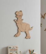 DIY MDF  dinosaur cutout wall decoration on a light gray wall with a book and pencils in the background.