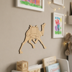 MDF DIY camel wall decoration on a beige wall with children's books and toys below.