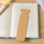 Brown bear-shaped  MDF DIY bookmark on an open book with a wooden surface underneath