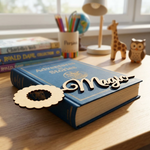 MDF DIY Bookmark 'Magic' on a book with a wooden cutout heart, surrounded by books and toys on a wooden surface.