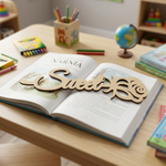 Open book with decorative MDF DIY  word 'Sweet' on a wooden table in a classroom setting.