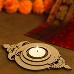 Decorative mdf candle holder with a lit candle on a brown surface with blurred orange flowers in the background.