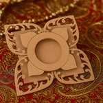 Laser-cut floral MDF tea-light holder with ornate petal design on decorative red and gold fabric