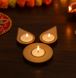 Three lit candles in decorative holders on a dark surface with blurred floral decorations in the background.