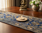 Decorative blue and gold table runner on a wooden table with a mdf tealight candle holder and statue.