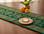 Decorative teal table runner with gold patterns, a candle, and flowers on a wooden table with mdf candle holder.